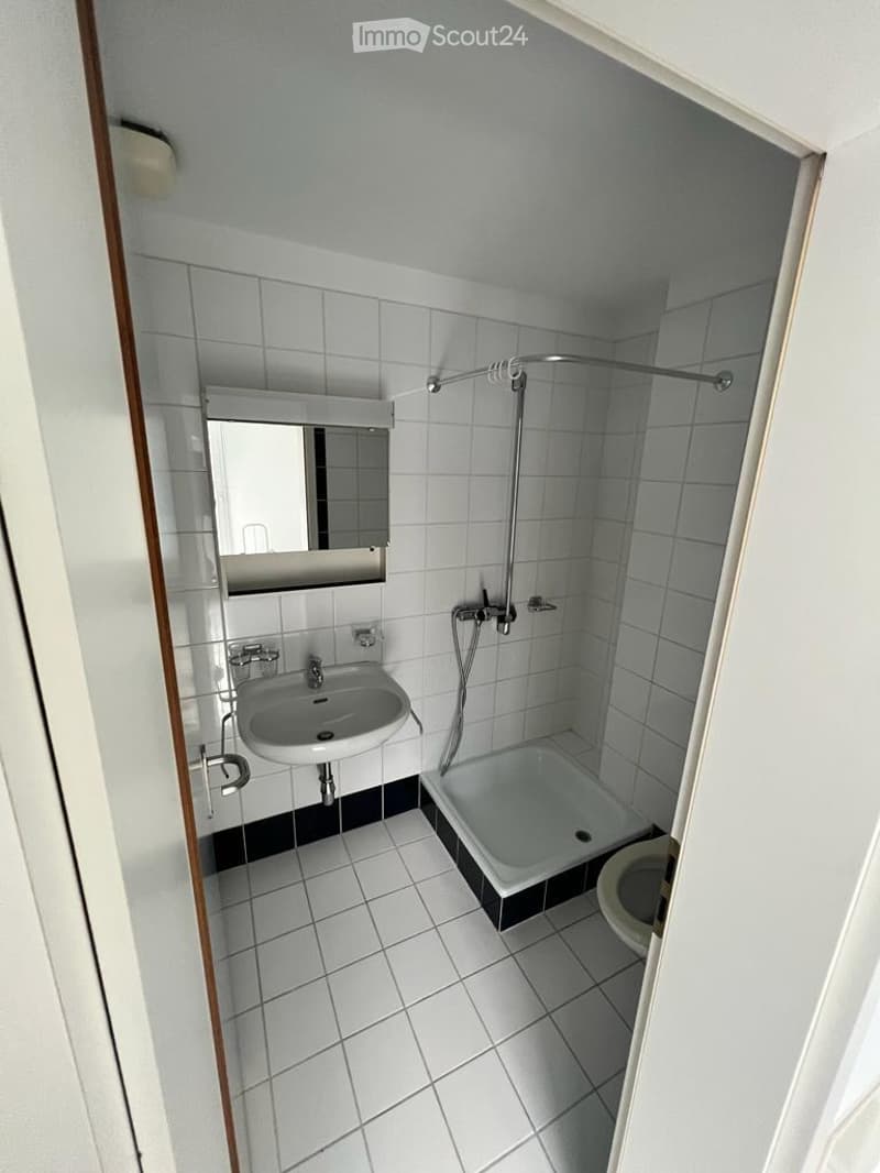 Small bathroom with white tiled walls and floor, featuring a sink, mirror, bathtub, and toilet.