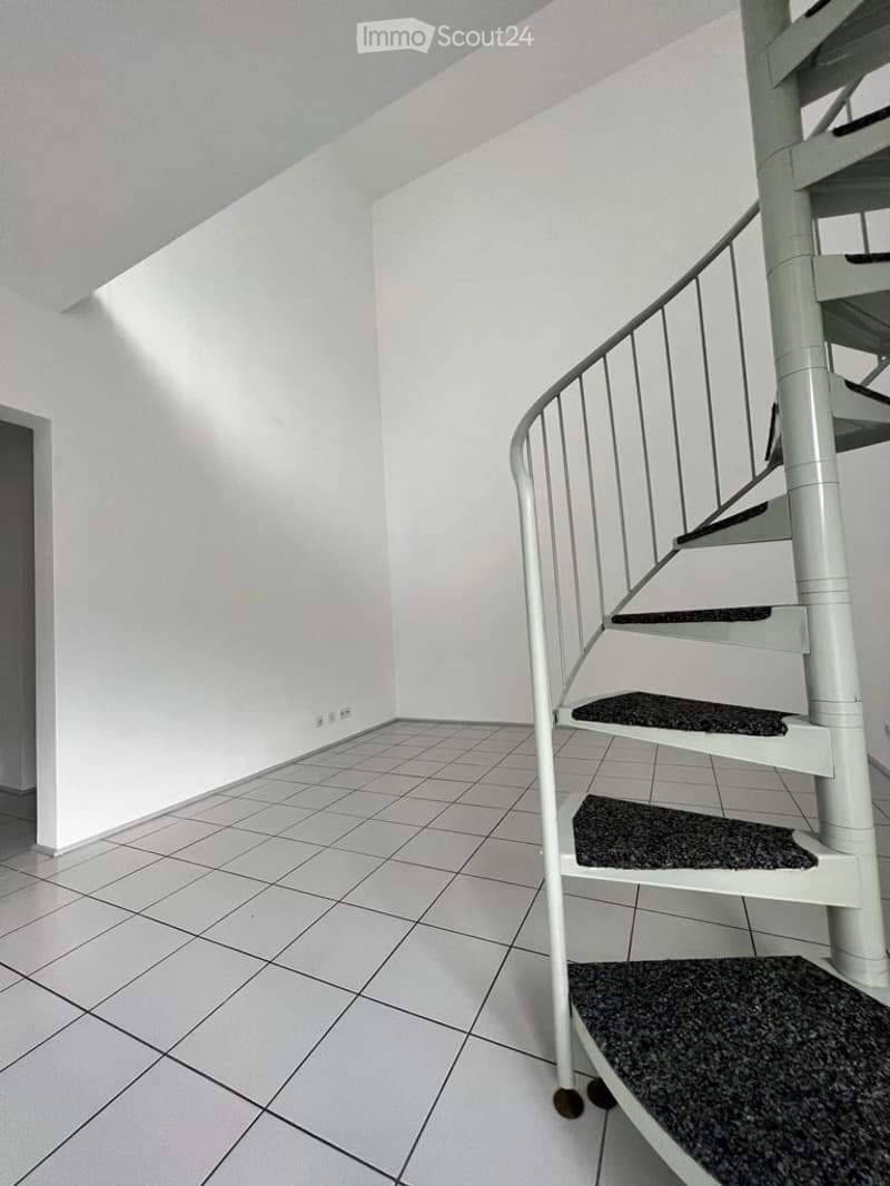 Empty room with white walls, tiled floor, and a spiral staircase leading upwards.