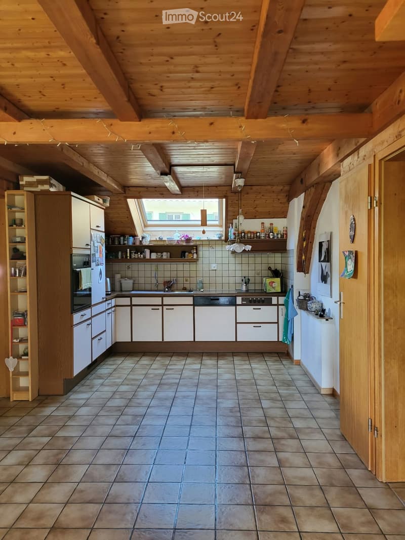 Bright kitchen with wooden beams, white cabinets, tiled floor, and various appliances including a refrigerator, oven, and dishwasher. Shelves hold kitchen items and decorative objects.