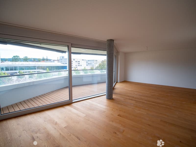 Empty room with wooden flooring, large glass sliding doors leading to a balcony, and a view of the cityscape.
