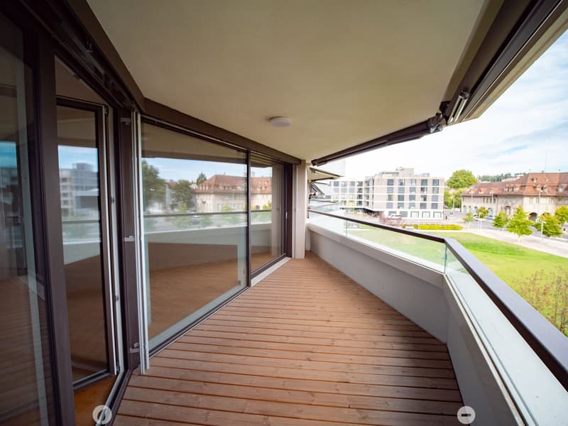 Balcony with wooden decking, large glass sliding doors, and a view of the city and greenery.