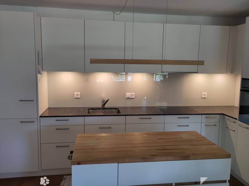 Modern kitchen with white cabinets, wooden countertop, stainless steel sink, and built-in lighting.