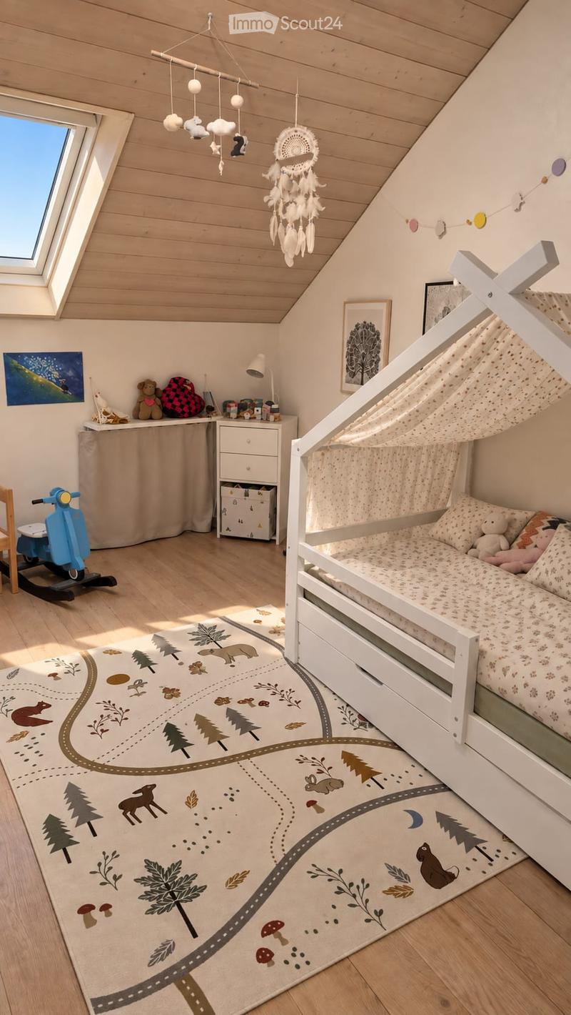 Cozy children's bedroom with a white wooden bed, nightstand, lamp, and various toys. Features a large, illustrated rug with forest and animal designs, and a dreamcatcher hanging from the ceiling.
