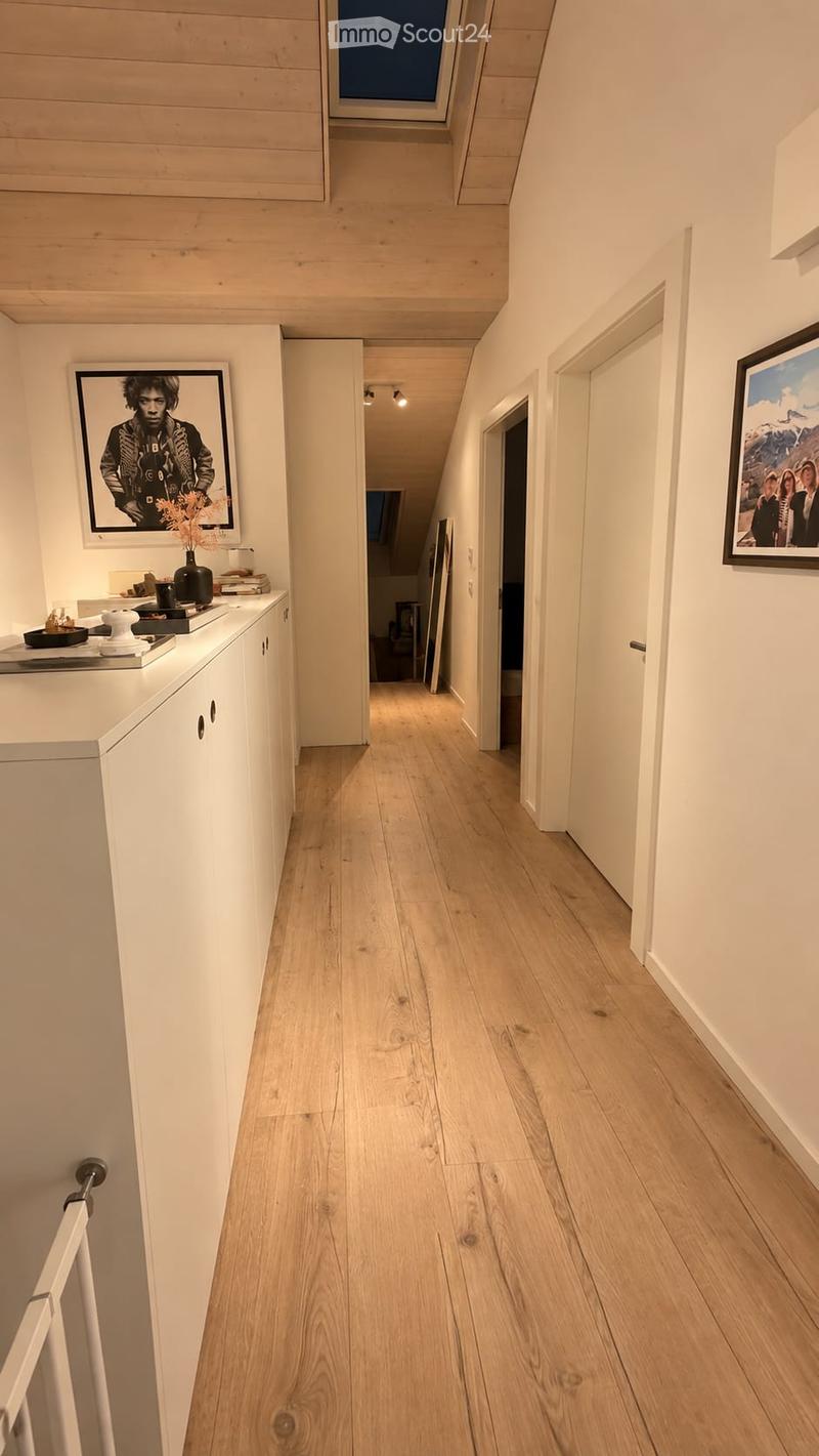 Modern hallway with light wooden flooring, white walls, and built-in storage unit on the left side. Features framed artwork and a small decorative arrangement on the storage unit.