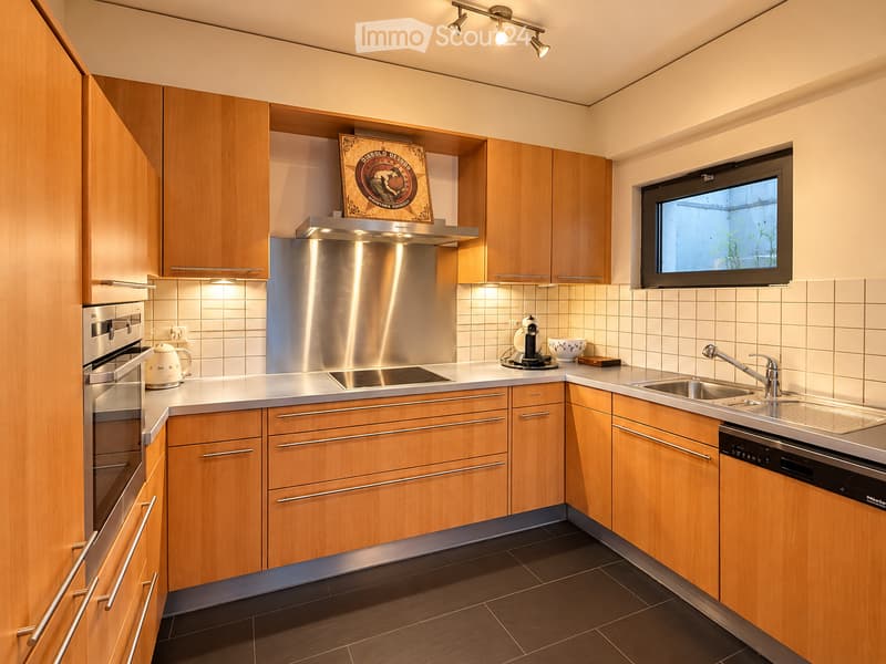 Modern kitchen with wooden cabinets, stainless steel appliances, induction stove, range hood, sink, and coffee maker on the counter.
