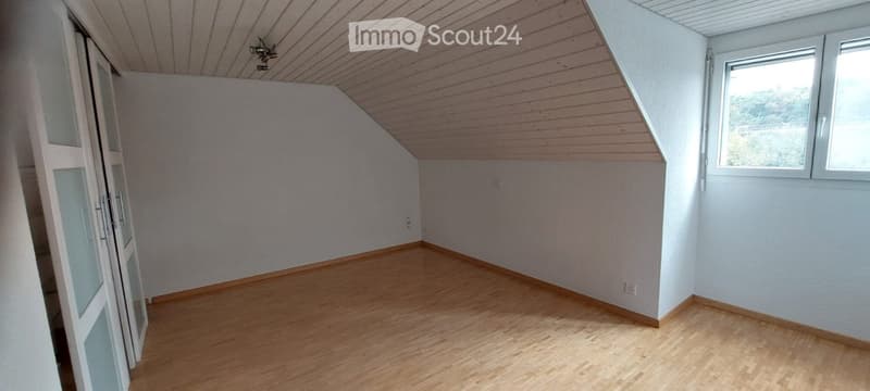 Empty attic room with wooden floor, slanted wooden ceiling, and large windows. No furniture or equipment present.