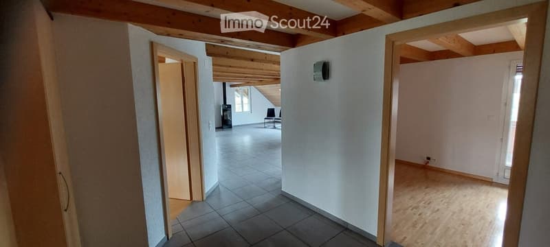 Empty room with exposed wooden beams, tiled floor, and a fireplace visible in the background.