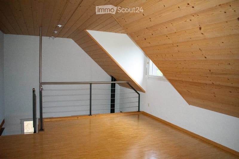 Modern hallway with wooden flooring, white walls, and a metal railing leading to an upper level. The ceiling features exposed wooden beams and recessed lighting.