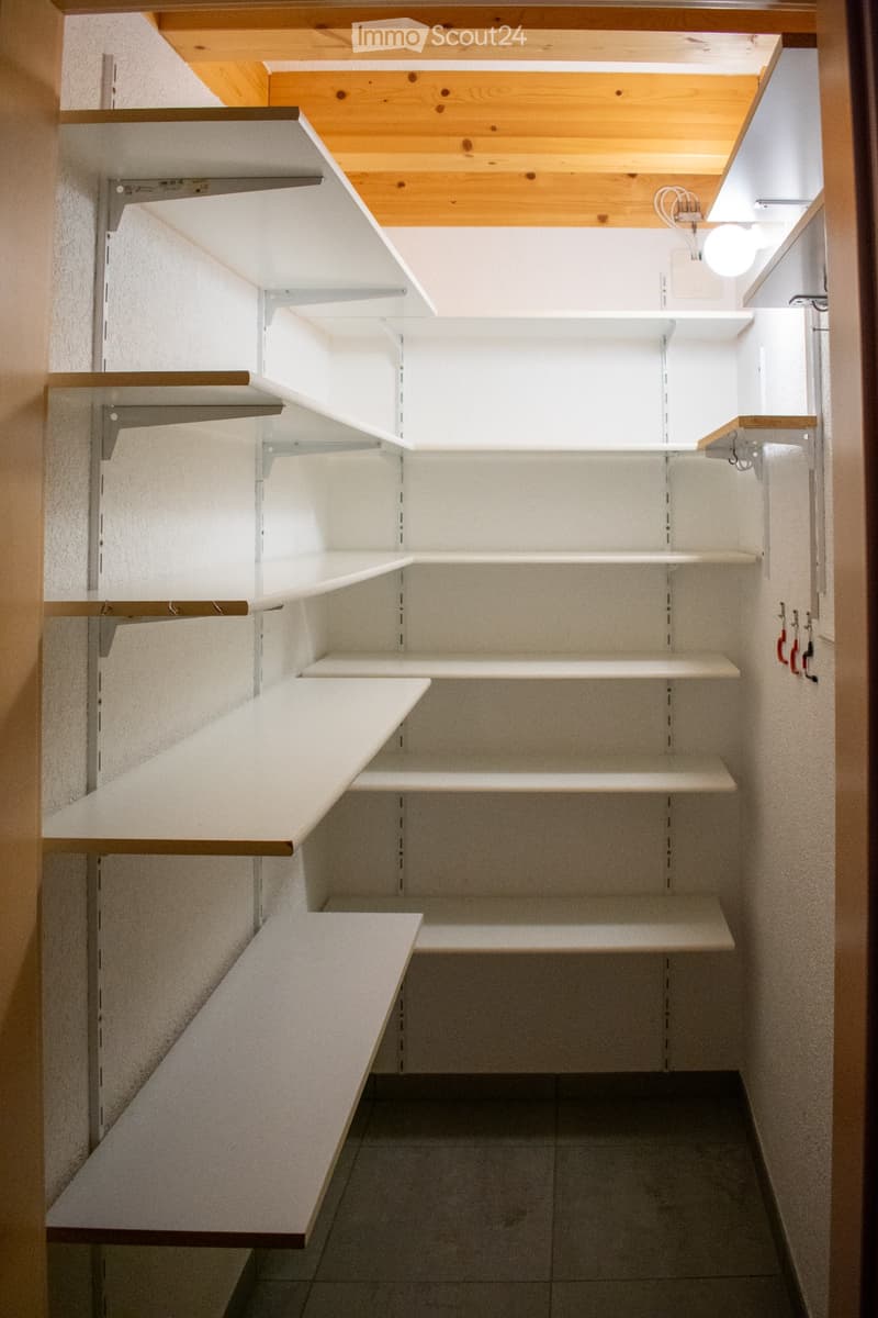 Empty closet with multiple white shelves and wooden trim, featuring a slanted wooden ceiling and tiled floor.