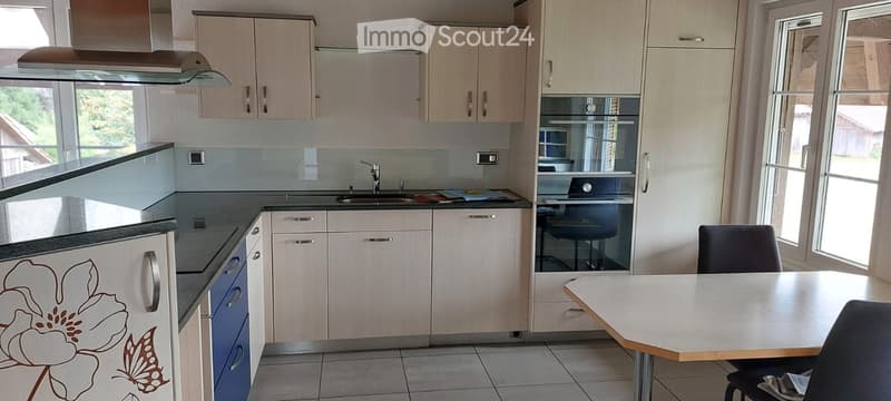 Modern kitchen with light wood cabinets, stainless steel sink, built-in oven, and a small dining area with a table and chairs.