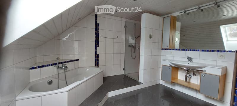 Modern bathroom with a bathtub, sink, mirror, and shower area. Features white tiles, dark flooring, and built-in cabinets.