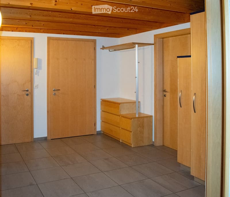 Empty room with wooden doors, built-in closet, and a small wooden chest of drawers. The room has tiled flooring and white walls.