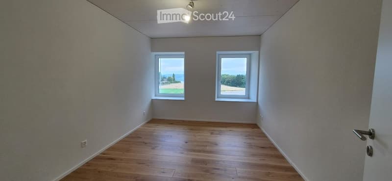 Empty room with wooden flooring, two windows offering a scenic view, and a single door.