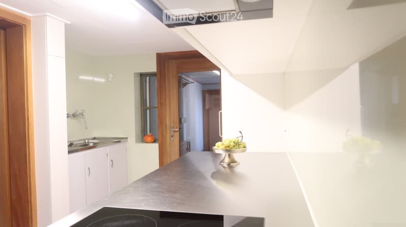 Modern kitchen with white cabinets, stainless steel sink, and a countertop with a bowl of grapes and an orange.