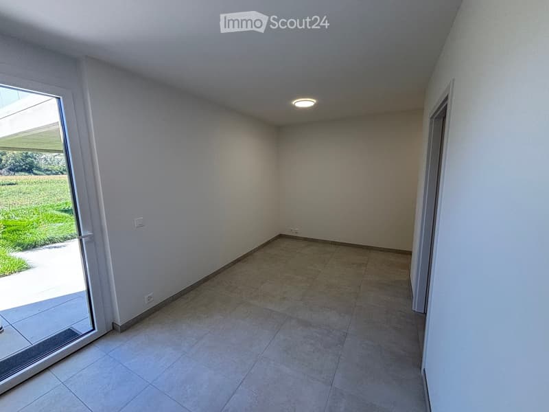 Empty room with tiled floor, white walls, large sliding glass door leading to a grassy outdoor area, and a ceiling light fixture.