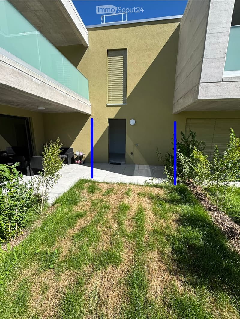 Modern house exterior with a small garden area, concrete pathways, and a patio with outdoor furniture.