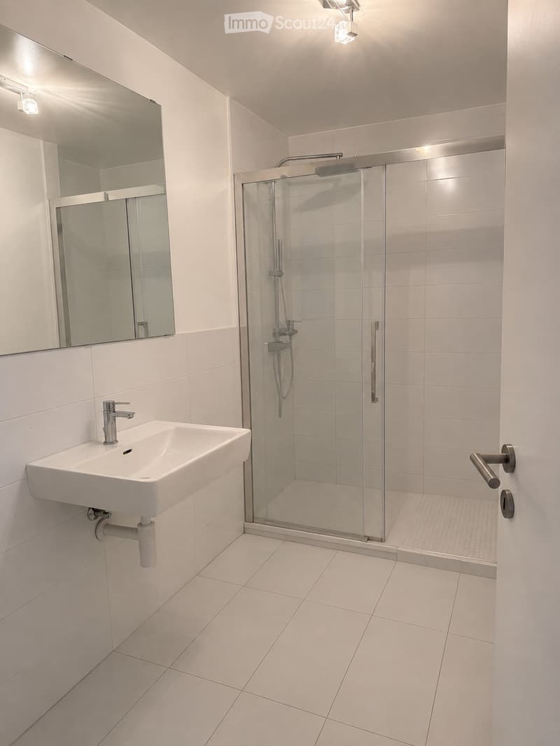 Modern bathroom with white tiles, a glass-enclosed shower stall, a wall-mounted sink with a modern faucet, and a large mirror above the sink.