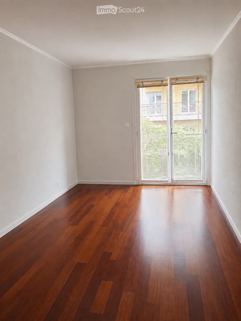 Empty room with wooden flooring and white walls, featuring a large sliding glass door leading to a balcony.