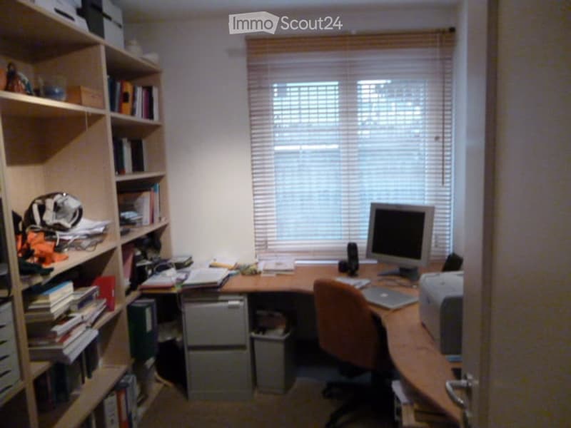 Home office with desk, monitor, printer, chair, bookcase, drawers, window with blinds.