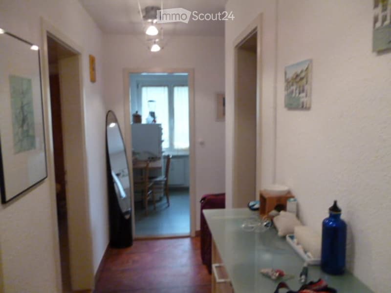 Corridor with hardwood floors, white walls, two picture frames, mirror, kitchen table with chairs, and refrigerator