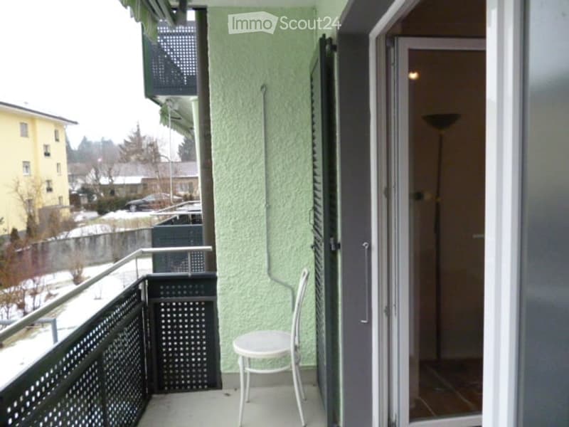 a balcony with railing, chair and sliding door with light