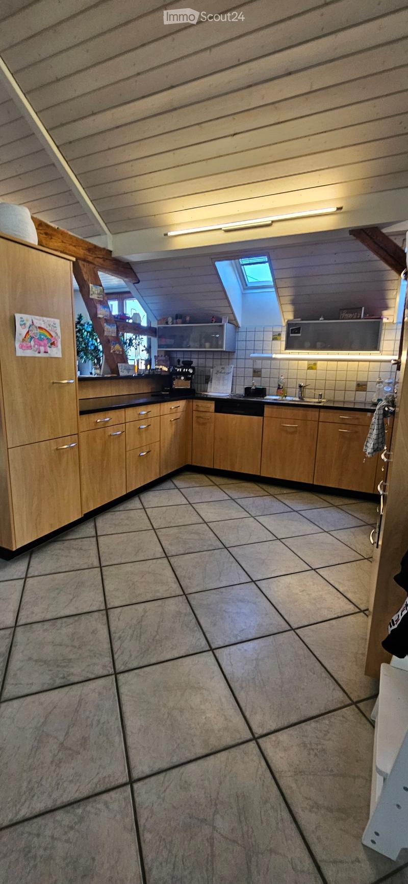A well-lit kitchen with wooden cabinets, a tiled floor, and various appliances including a microwave, coffee maker, and oven. There is a sink with a faucet and a towel hanging nearby.