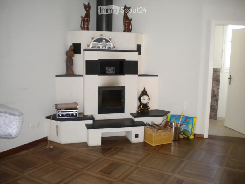 Modern fireplace with decorative items, including cat statues, a clock, and a suitcase on the mantel. Wooden floor and white walls.