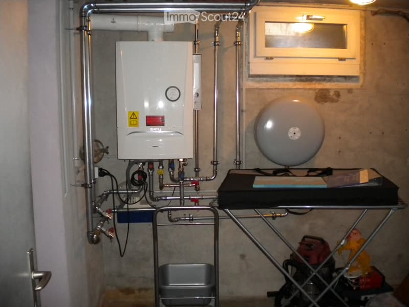 Utility room with a water heater, water tank, table, stool, and trash bin.