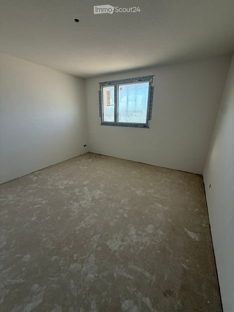 Empty room with bare walls and unfinished concrete floor, featuring a single window with metal frame.