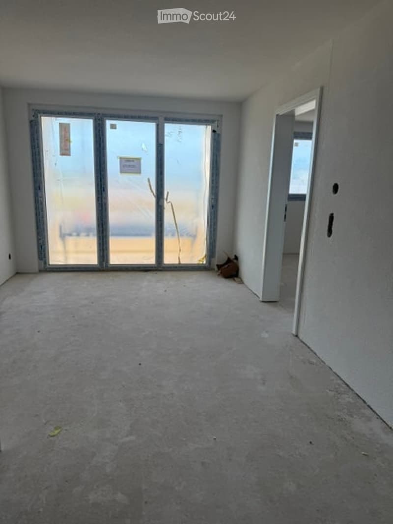Empty room with bare walls, concrete floor, large glass sliding doors, and an open doorway leading to another space.