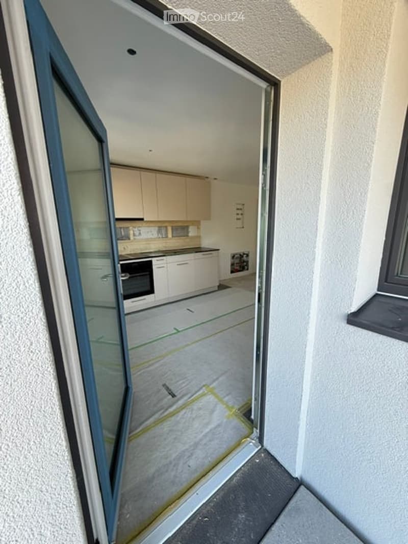 Empty kitchen with white cabinets, stainless steel appliances, and a tiled floor, viewed through an open glass door.
