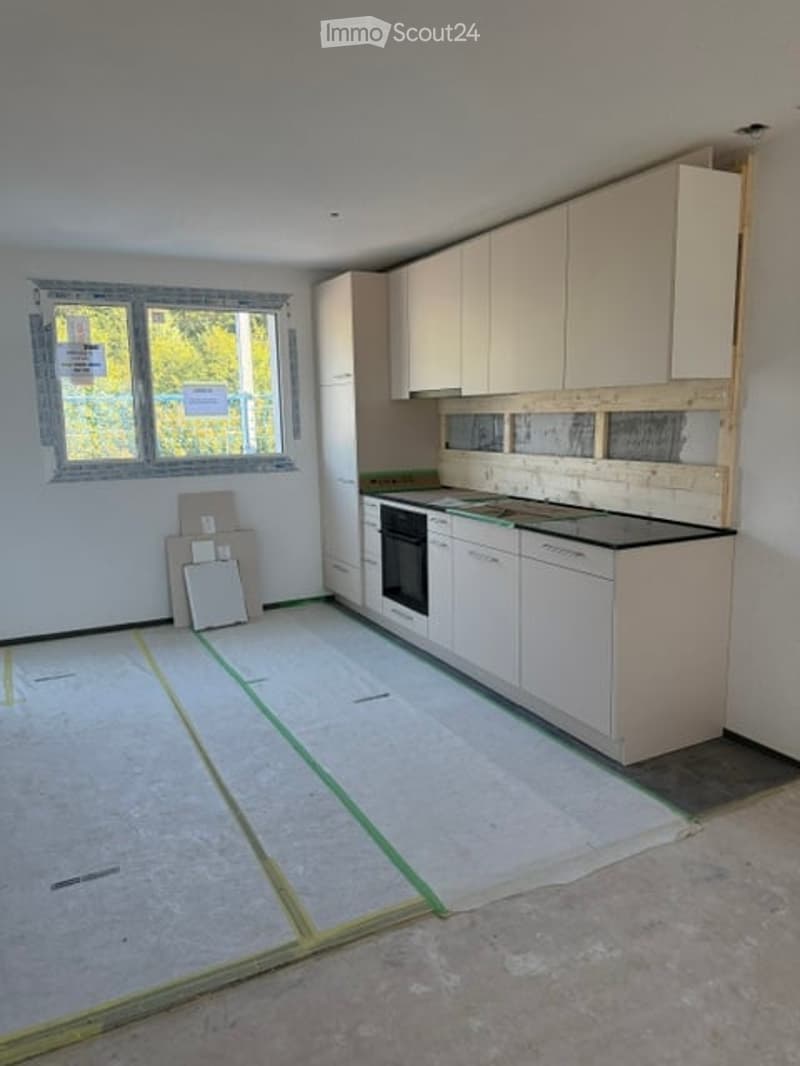 Empty kitchen with white cabinets, black countertop, and a window. Floor is under renovation with protective sheets.
