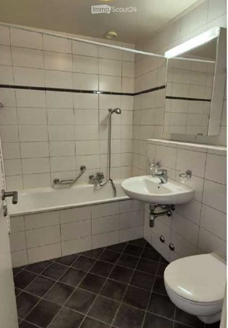 Modern bathroom with white tiled walls, black accent border, bathtub, sink, toilet, and mirror.