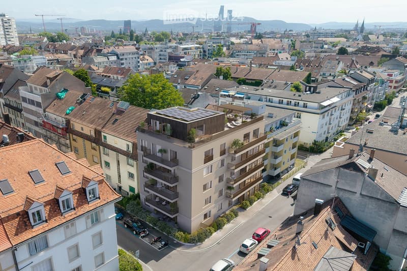 Aerial view of a dense urban neighborhood with multiple residential buildings, red-tiled roofs, balconies, and surrounding greenery.