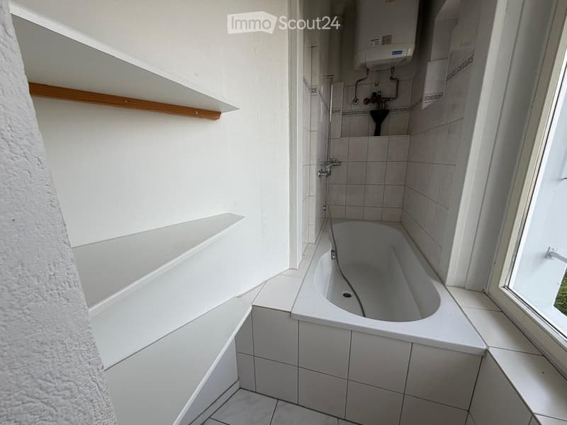 Modern bathroom with a bathtub, shower area, tiled walls, and built-in wooden shelves.