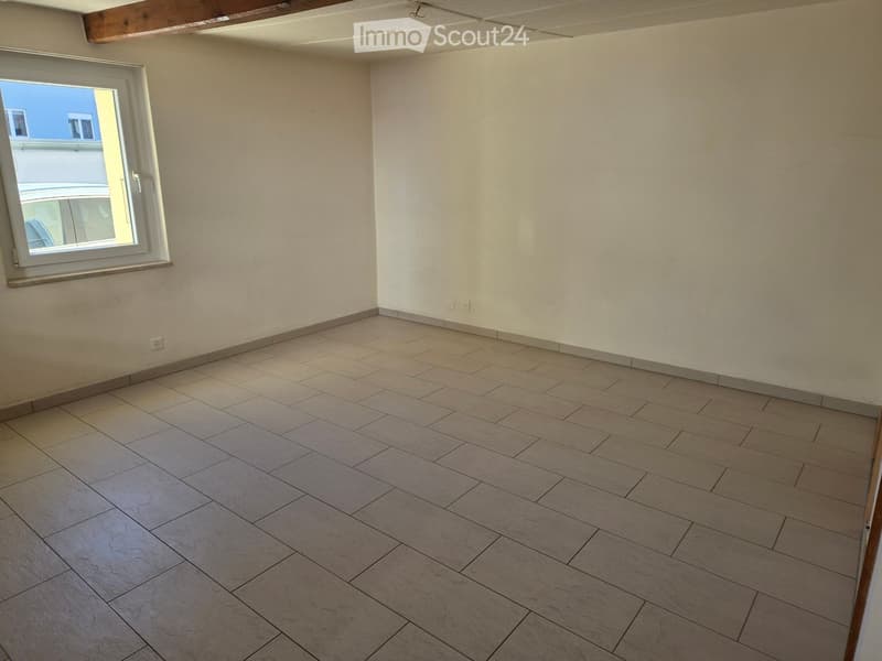 Empty room with tiled floor and white walls, featuring a large window with white frame and a view of the outside.