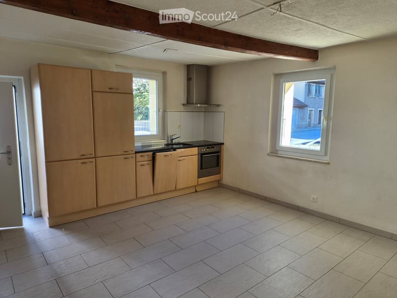 Empty kitchen with light wooden cabinets, stainless steel appliances, and tiled flooring.