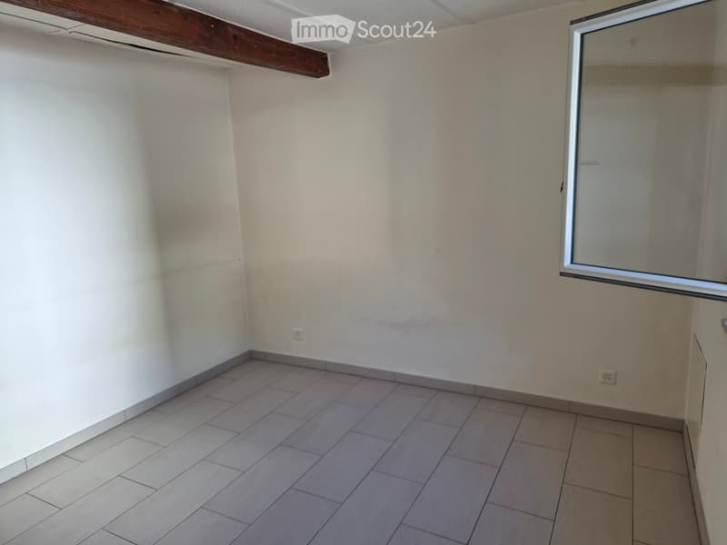Empty room with tiled floor, white walls, and a single window with a metal frame. No furniture or equipment is present.