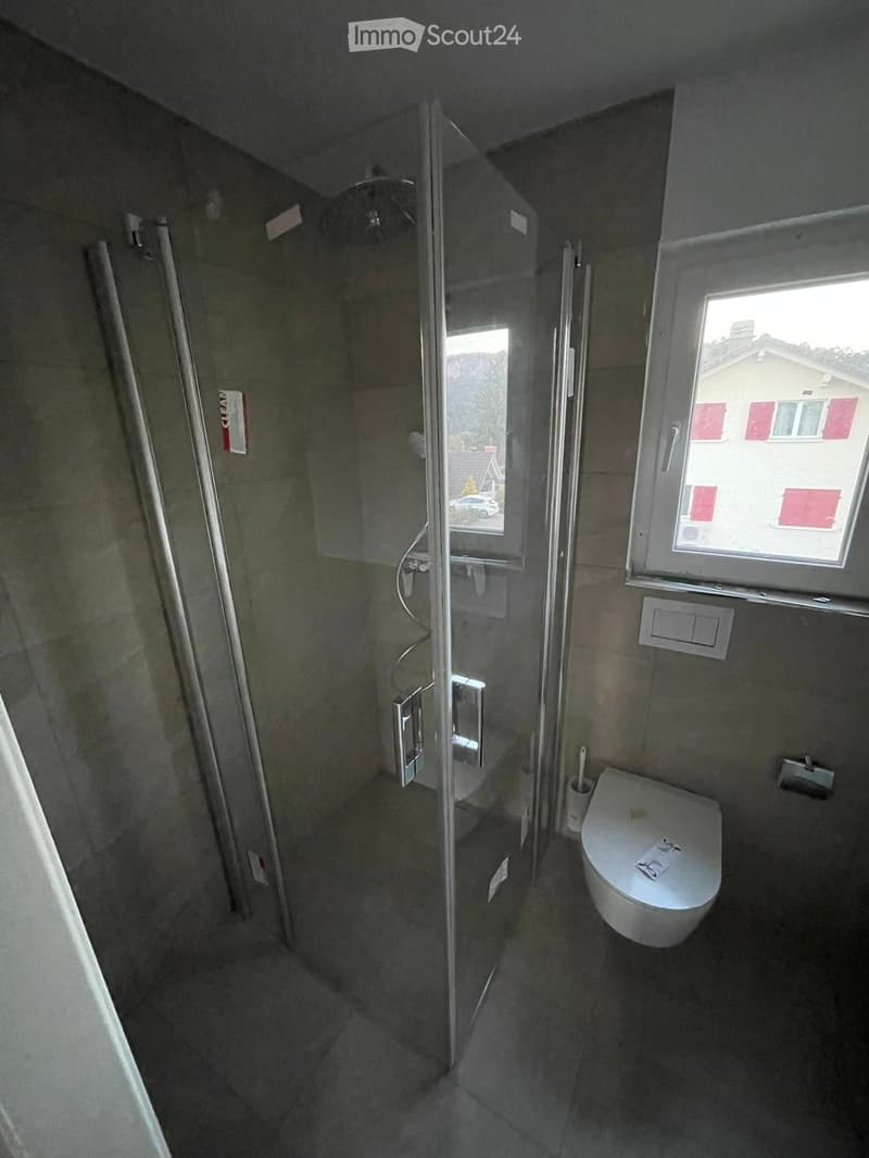 Modern bathroom with a toilet, glass-enclosed shower, and a window providing natural light.