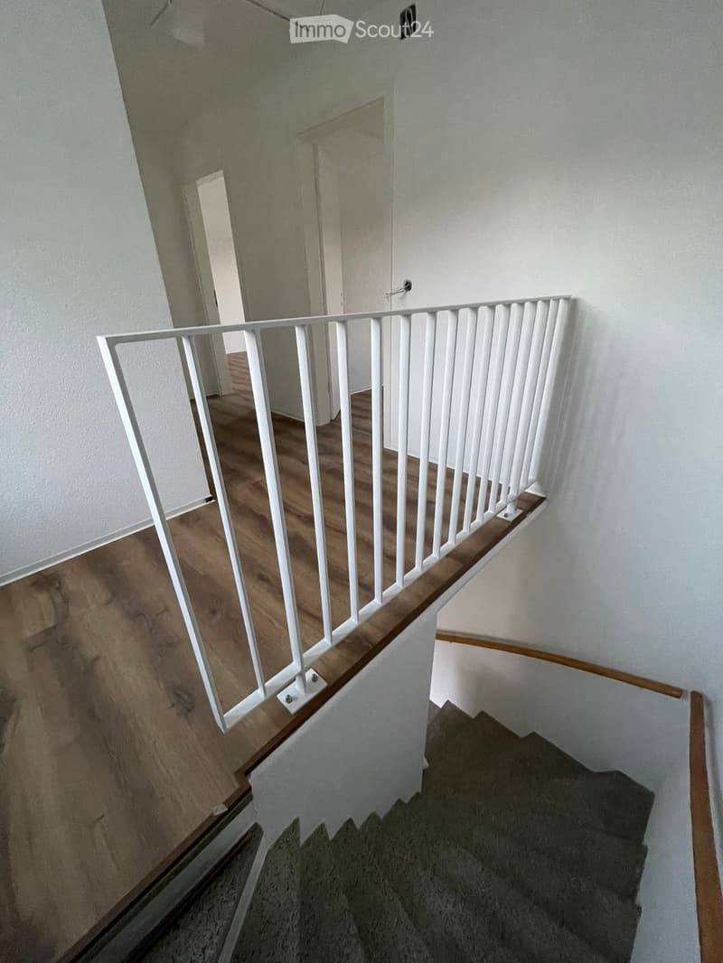 Wooden staircase with white railing and gray carpeted steps, leading to an open doorway.