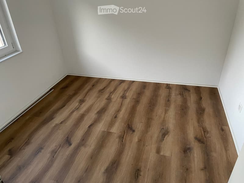 Empty room with light-colored walls and a polished wooden floor, featuring a single window on one wall.