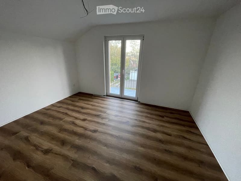 Empty room with wooden flooring and white walls, featuring a large sliding glass door leading to a balcony.