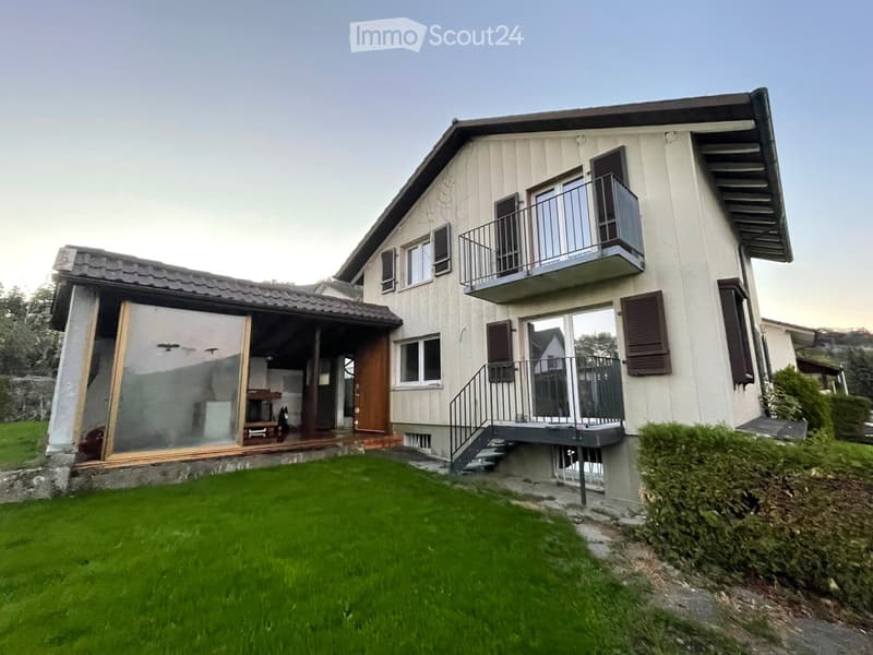 Two-story house with a balcony, wooden shutters, and a well-maintained lawn.