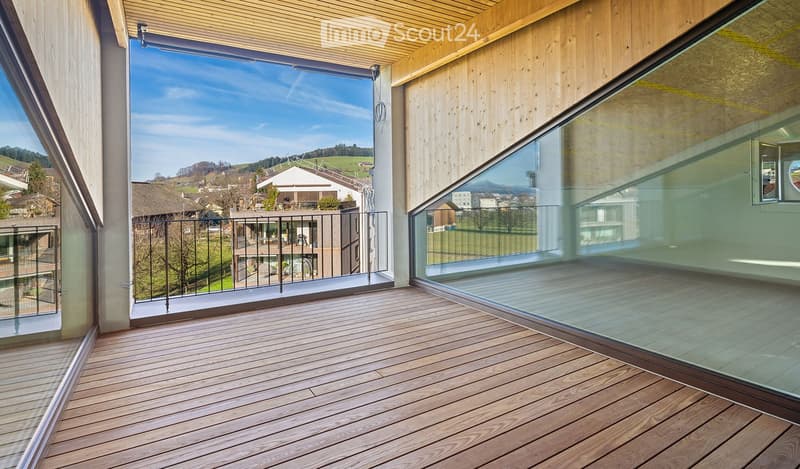 Modern wooden balcony with glass railings, overlooking a scenic countryside view.