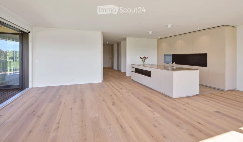 Modern kitchen with light wood flooring, white cabinets, a central island, and a large window offering a view of the outdoors.
