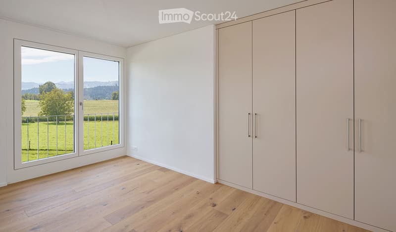 Empty room with light wooden flooring, white walls, large sliding glass doors leading to a balcony, and built-in wardrobes.