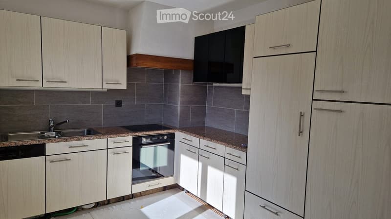 Modern kitchen with light wood cabinets, granite countertop, stainless steel sink, oven, and dishwasher.