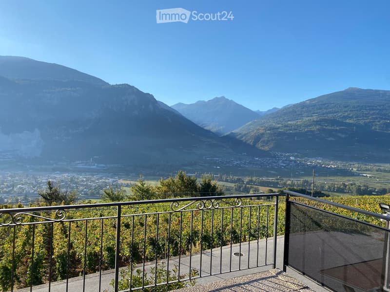 Balcony with metal railing overlooking a scenic valley and distant mountains.