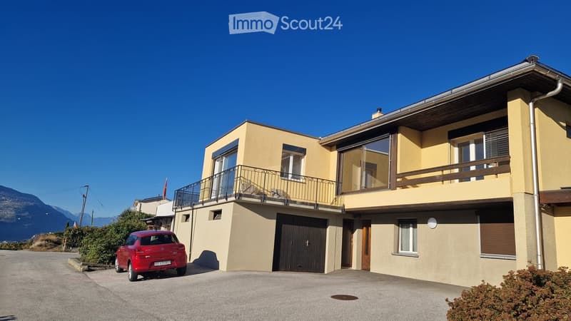 Two-story house with yellow walls, large windows, balcony, garage, and parking space.
