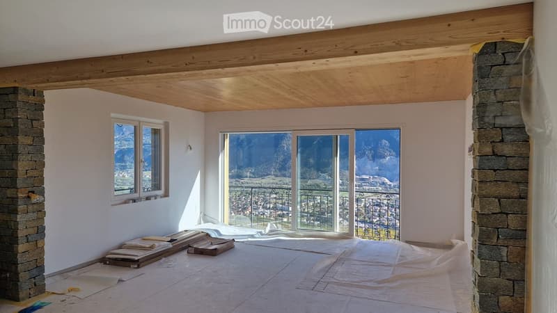 Empty room with wooden ceiling, stone pillars, large windows, and a scenic mountain view. Floor covered with protective sheets.